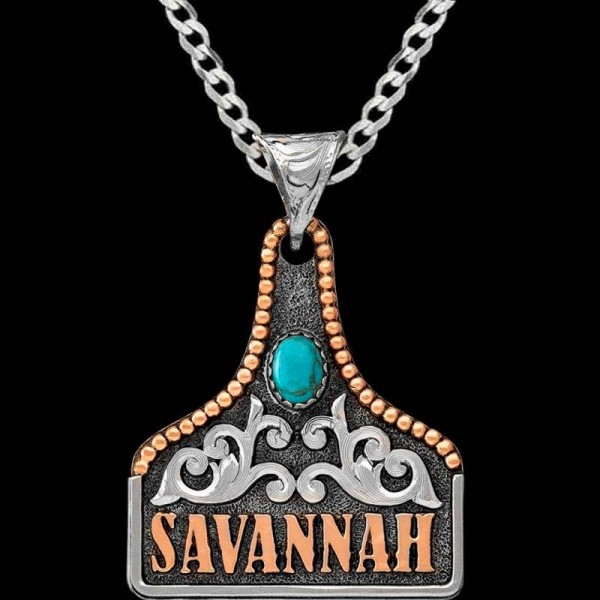 The Storm Cow Tag Necklace features a touch of antique allure, adorned with silver scrollwork copper letters and a charming bead edge, accentuated by an oval turquoise stone. Order it now!